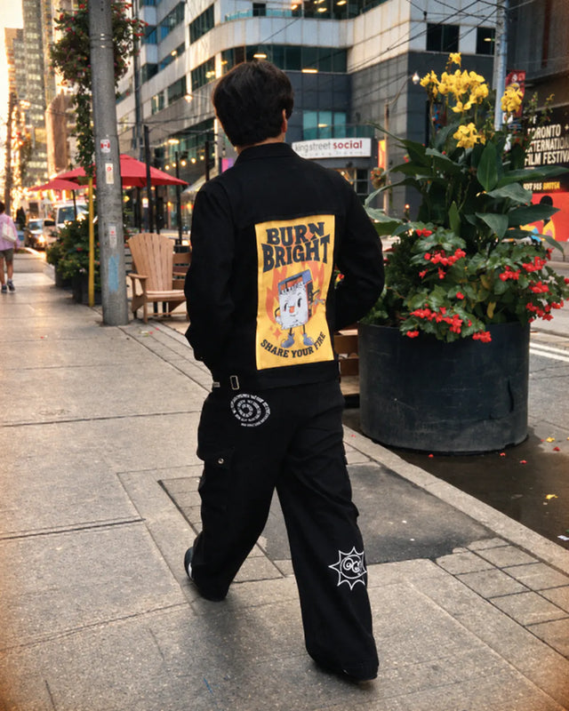 Person walking in a black jacket with a yellow Burn Bright art panel.