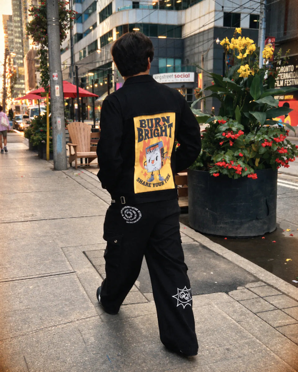Person walking in a black jacket with a yellow Burn Bright art panel.