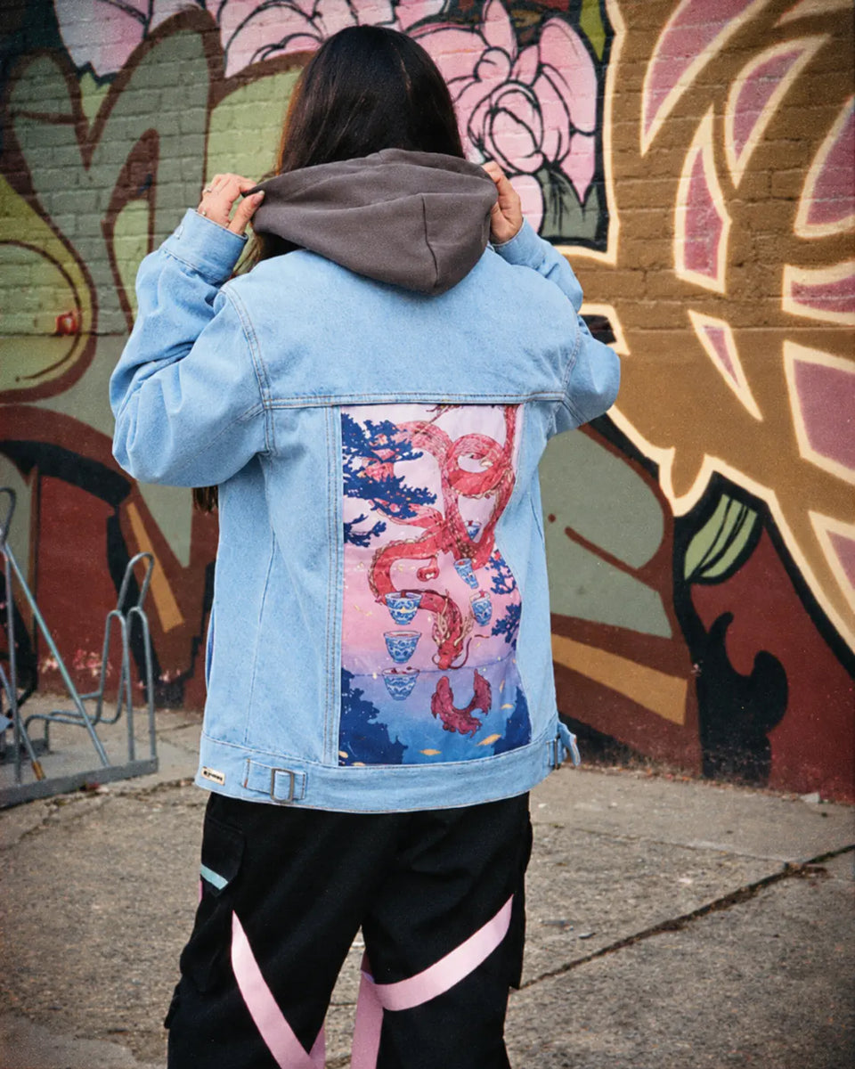 Back of a blue denim jacket with a pink dragon art panel in front of a mural.