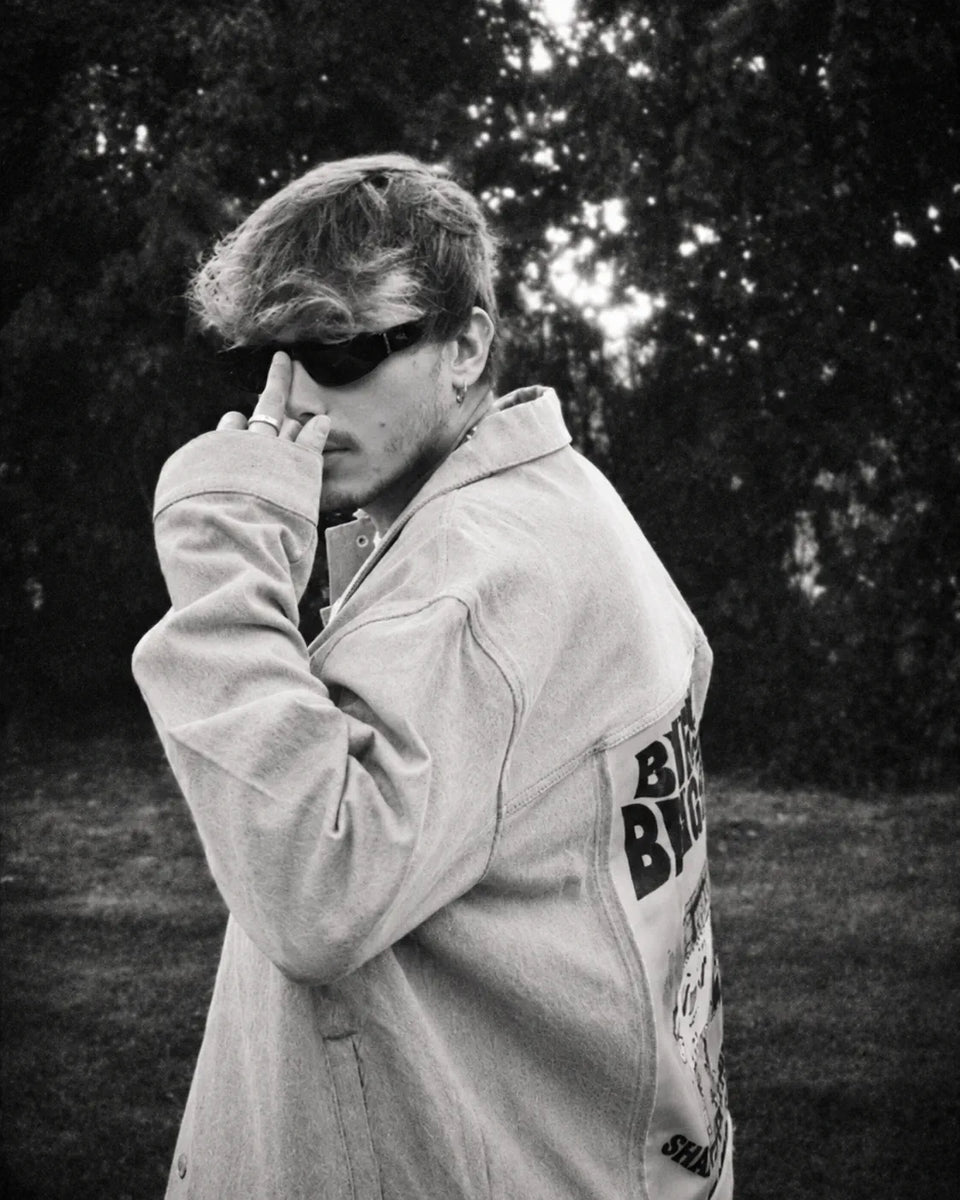 Black-and-white portrait of a person in sunglasses and a light jacket with a back art panel.