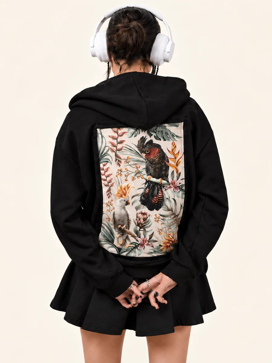 After Hours Hoodie with Parrot’s Paradise Light art, worn by a woman in headphones hands clasped behind her back.