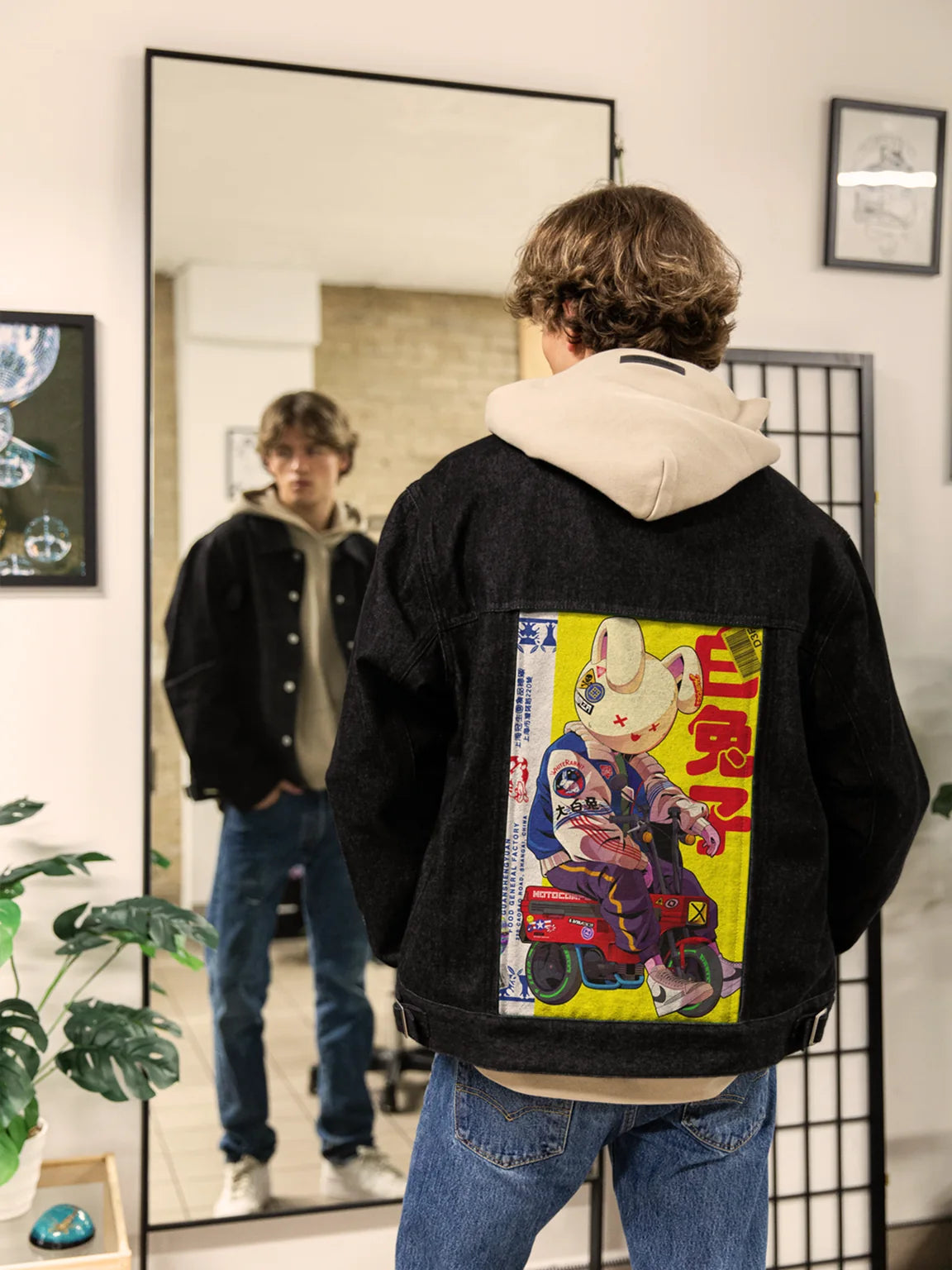Man wearing a Raven denim jacket over a light hoodie, showing rabbit artwork in a mirror.