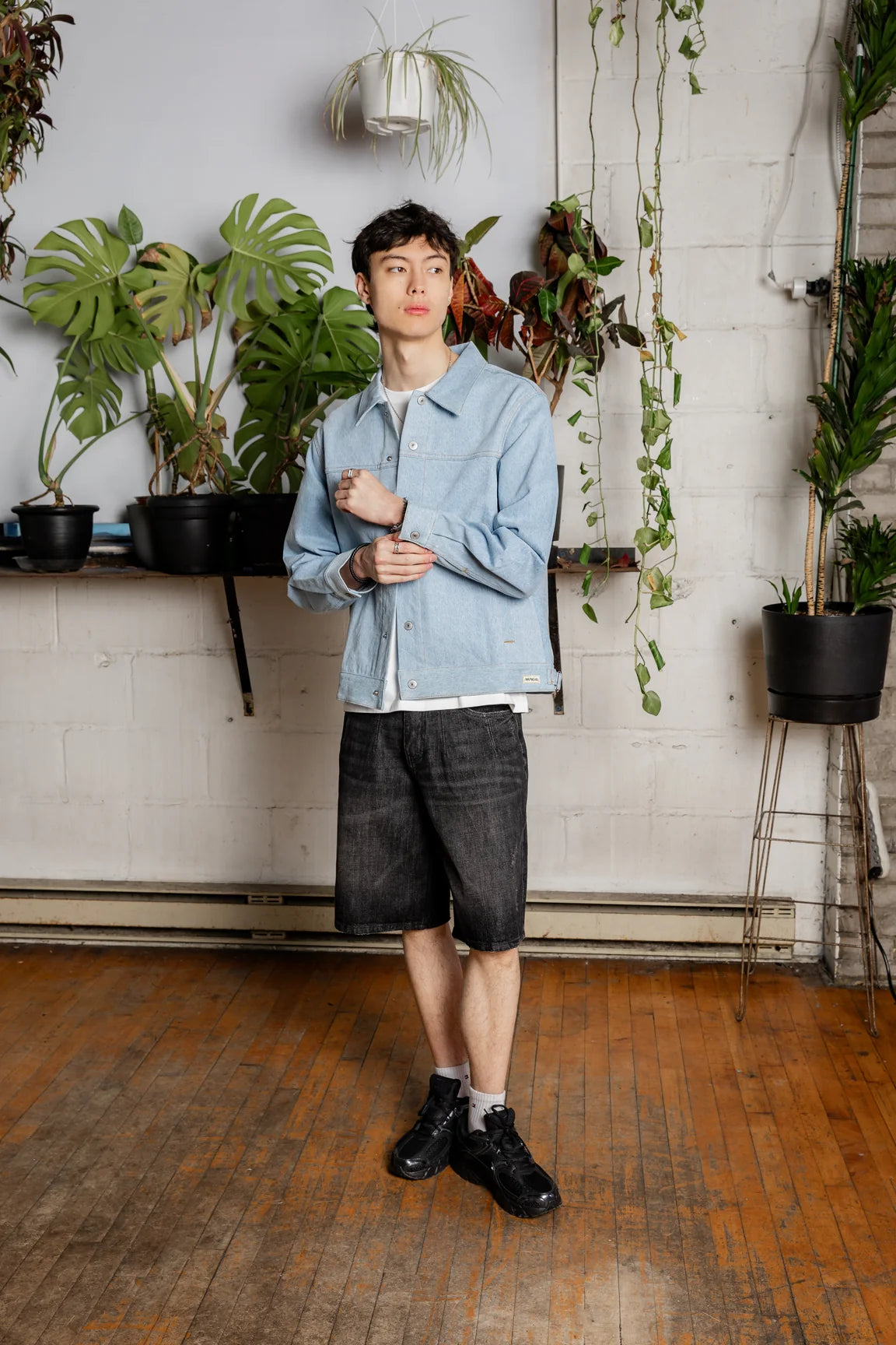 Man wearing the front of an Oceanside denim jacket and dark denim shorts in a plant-filled studio.