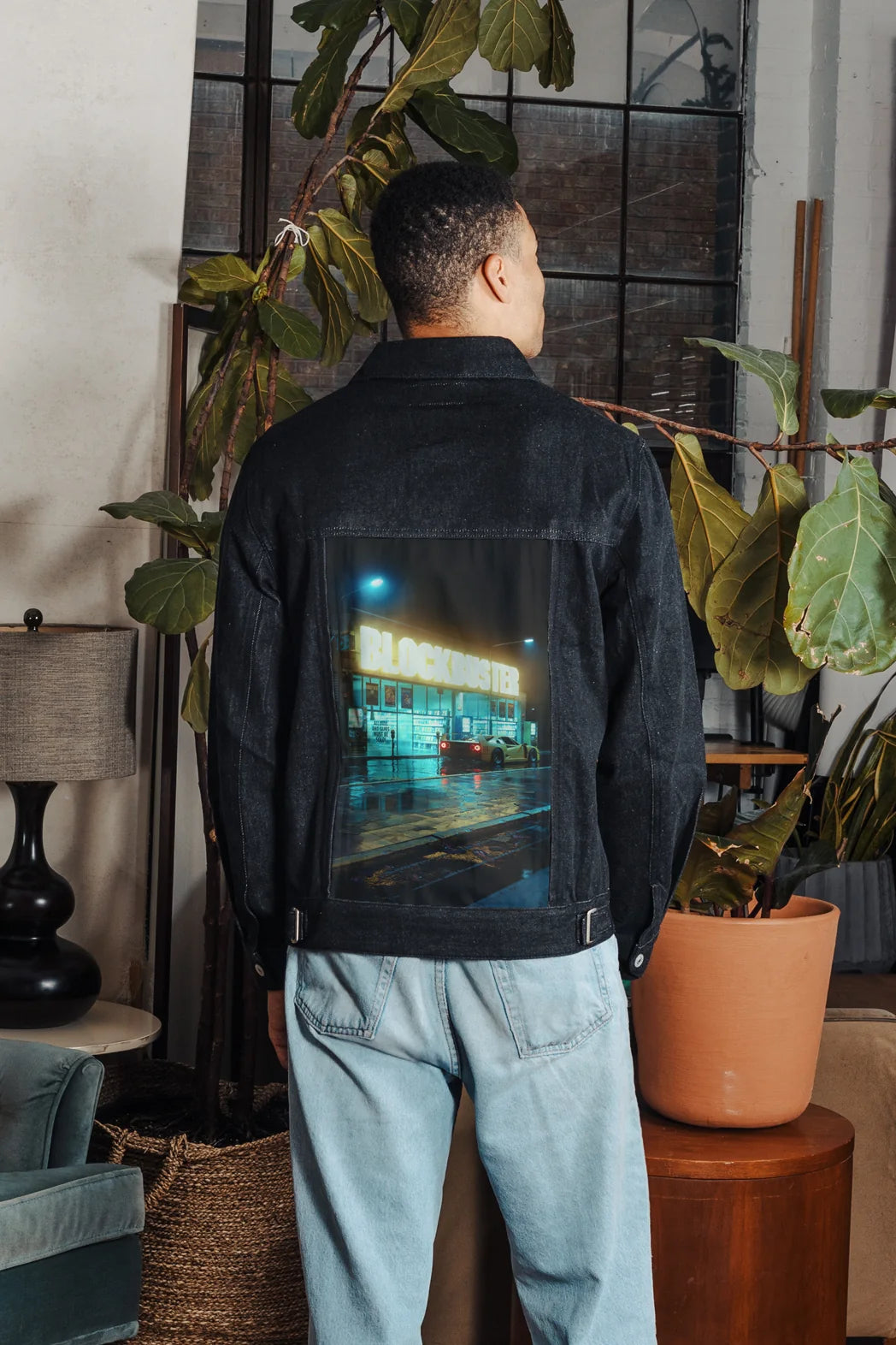 Man wearing a Raven denim jacket with nighttime video-store artwork on the back.