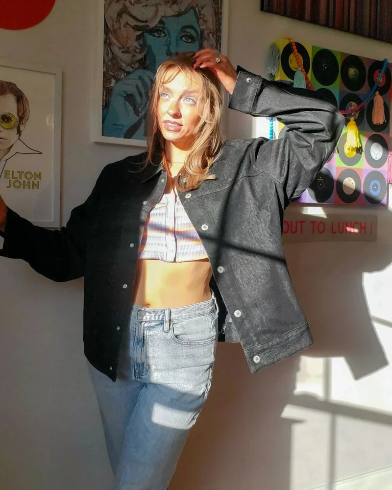 Creator wearing the front of a Raven denim jacket and light jeans in a sunlit room with music artwork.