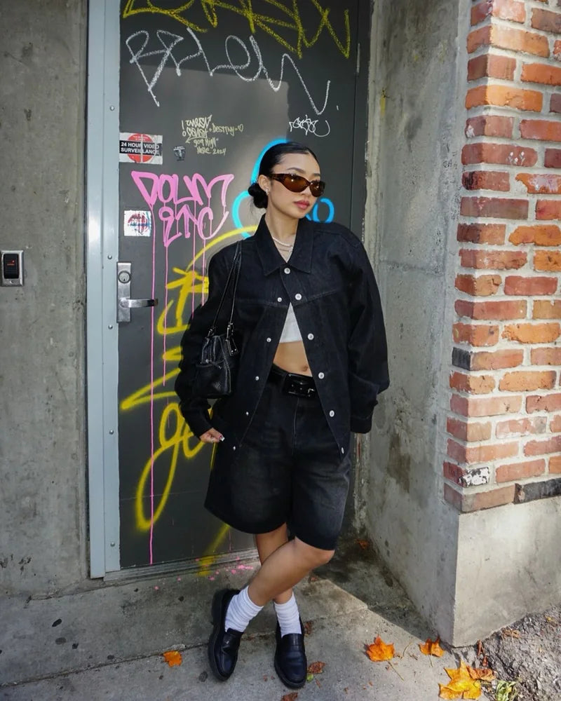 Creator wearing the front of a Raven denim jacket with sunglasses and black shorts beside a graffiti door.