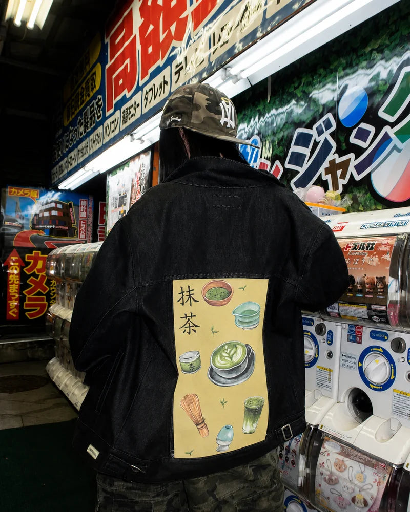 Creator wearing a Raven denim jacket with Matcha art beside capsule-toy machines.