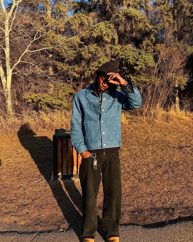 Creator wearing the front of a Blu Stone denim jacket over a dark hoodie on a sunny wooded path.