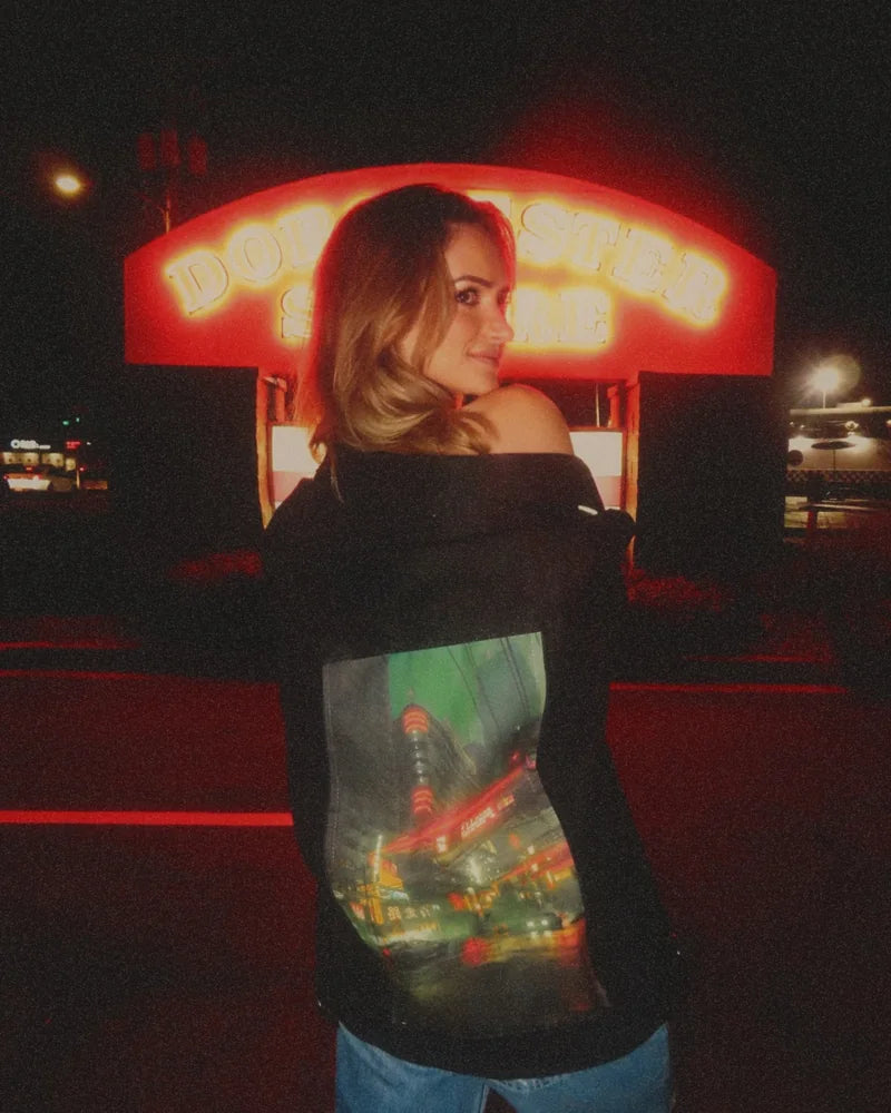 Creator showing nighttime city artwork on a Raven denim jacket beside a glowing red sign.