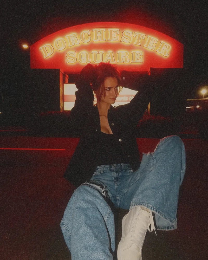 Creator wearing the front of a Raven denim jacket with ripped light jeans and white sneakers at night.