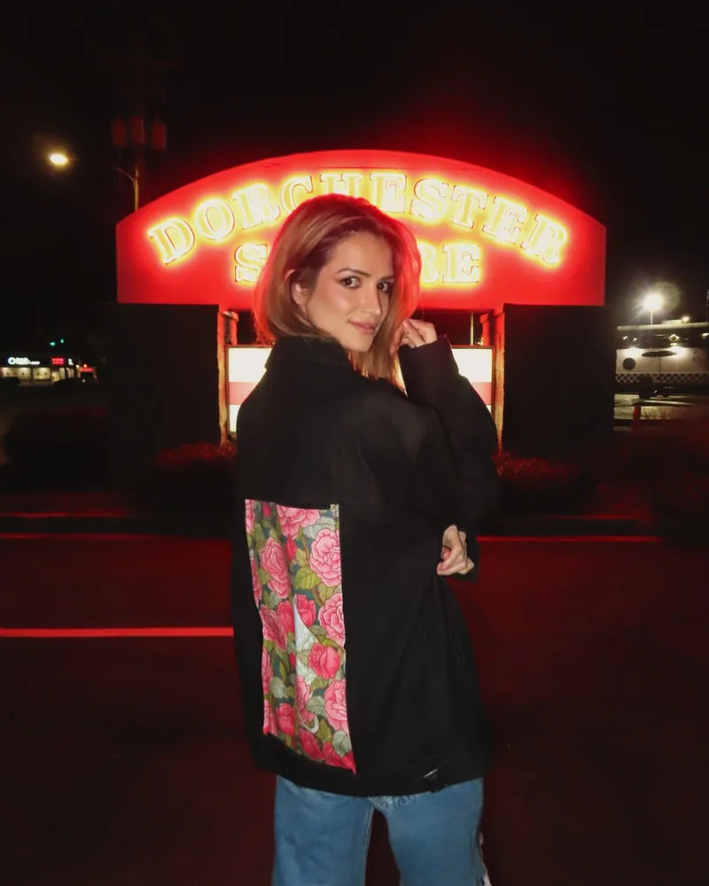 Creator wearing a Raven denim jacket with pink rose back art beside a glowing red sign at night.