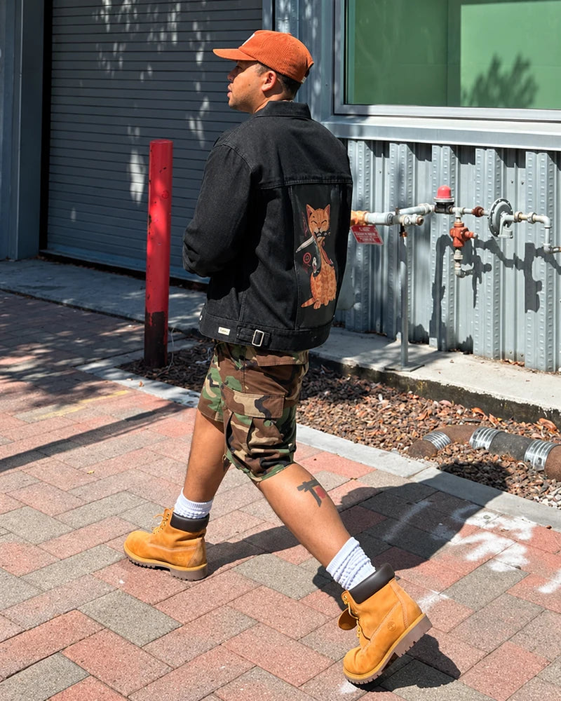 Customer walking along a sunny street in a Raven denim jacket with Catana art, camouflage shorts and tan boots.