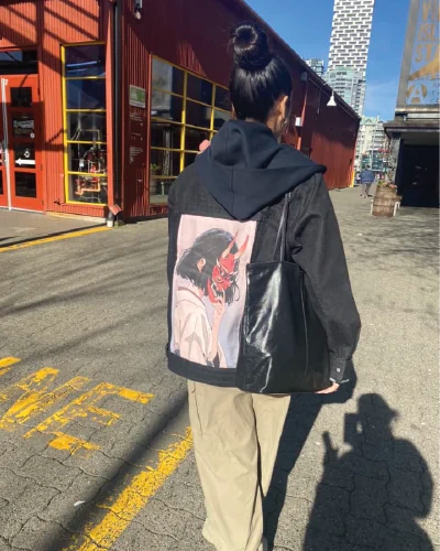 Customer styling a black OG Denim Jacket with Masked Oni art on a sunny street.