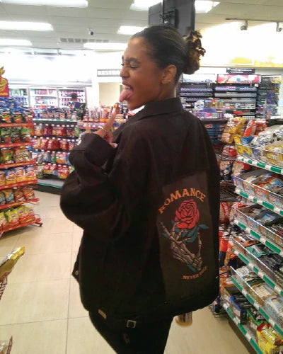 Customer styling a black OG Denim Jacket with Romance Never Dies art in a convenience store.